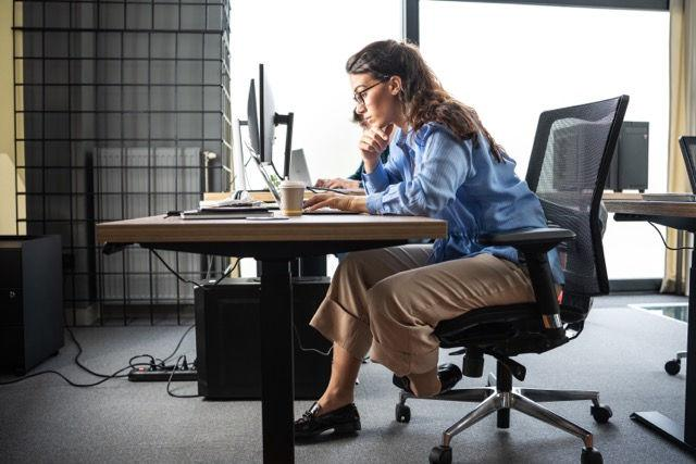 Woman sitting at office desk with forward head posture while working on computer