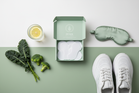 Wellness flat lay showing detox foot patches, a glass of water, fresh green vegetables, running shoes, and a sleep mask on a white and sage green background